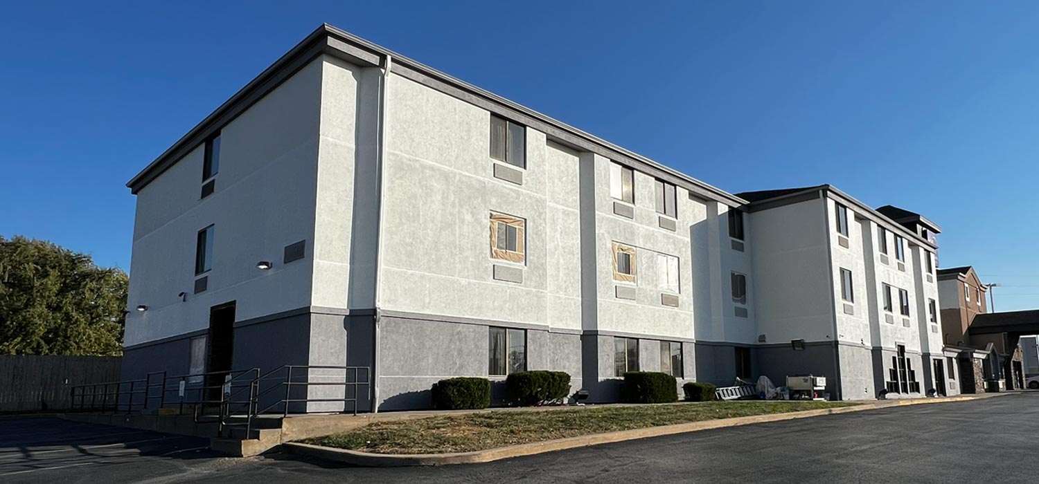 Three-story building mid-repaint with masked windows, handled by commercial painters in Topeka, KS