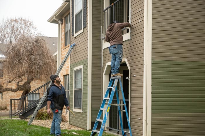 Crew on ladders prepping an apartment exterior for a painting company in Topeka, KS