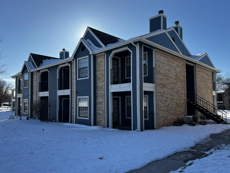 Two-story apartment building with navy siding and white trim on a snowy winter day